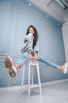 a woman sitting on top of a white stool next to a blue and gray wall