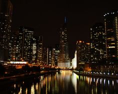 the city is lit up at night with lights reflecting in the water and skyscrapers