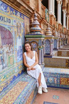 a woman sitting on the side of a building next to tiled walls and columns with colorful designs