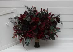 a bouquet of red flowers sitting on top of a white door frame with greenery