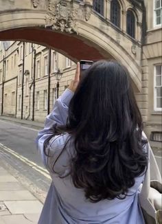 a woman is taking a photo with her cell phone in front of an arch on the street