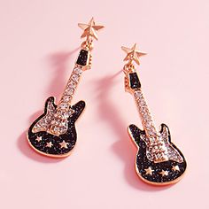 pair of black and white guitar shaped earrings with gold stars on them, against a pink background