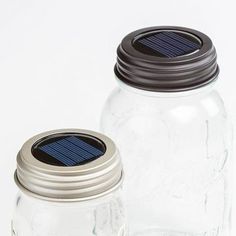 two mason jars with solar panels on the lids are sitting side by side in front of each other