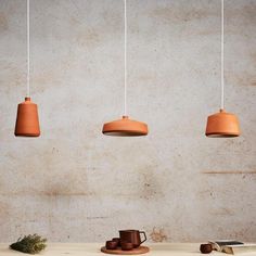 three orange hanging lights above a table with a book and cup on it next to a plant