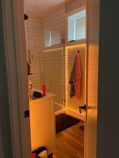 an open door leading into a bathroom with lights on the walls and wood flooring