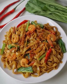 a white plate topped with pasta and shrimp on top of a table next to red peppers