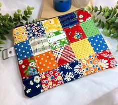 a colorful patchwork laptop case sitting on top of a table next to some flowers