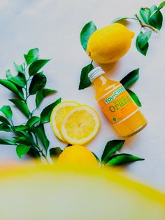 a bottle of orange juice next to some lemons and leaves on a white surface