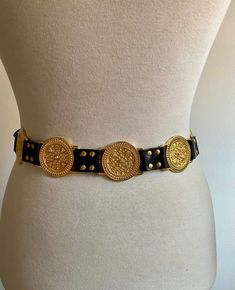 Vintage imitation leather belt with studs and medallions worked in gold-colored metal from the early 1990s. Reminiscent of the typical Versace belt of those years. It is a belt that has its own "weight", exactly 330 grams, given by the fact that it has 10 gold-colored medallions worked on the external side, one of which has the function of closing the belt. It's a belt that catches the eye. Worn very little, it is still in excellent condition. It only has a few micro marks on the edge of some of Vintage Belts Women, Vintage Leather Belt With Gold Buckle, Luxury Vintage Belts With Brass Hardware, Luxury Gold-tone Belt Buckle For Formal Wear, Luxury Gold Belt With Antique Buckle, Luxury Gold Belt With Brass Buckle, Versace Belt, Gold Belts, Vintage Belts