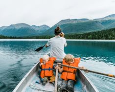 a woman and two children in a boat on the water with mountains in the background