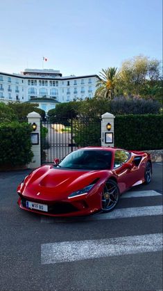 a red sports car parked in front of a gated entrance to a large building