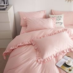 a pink comforter with ruffles and a pillow on the bed next to it