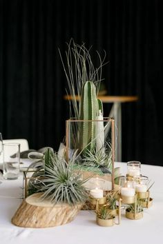 a table topped with candles and plants on top of a white table cloth covered table