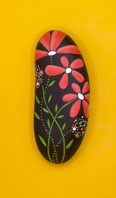 a painted rock with red flowers on it against a yellow background that looks like something out of nowhere