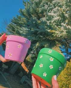 two people holding up plastic cups in front of some trees and grass with flowers on them