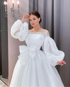 a woman wearing a white wedding dress with long sleeves and a bow on the waist