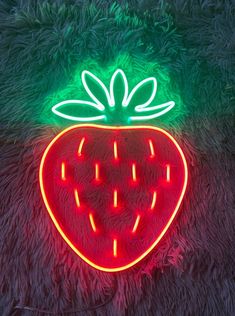 a neon strawberry sign sitting on top of a furry surface in front of a green background