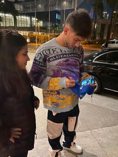 a man standing next to a woman on a sidewalk while looking at a cell phone