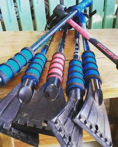 several different types of skis and poles on a wooden table with chairs in the background