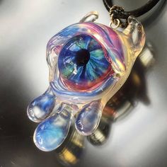 an eyeball shaped glass pendant on a black leather cord is hanging from a necklace