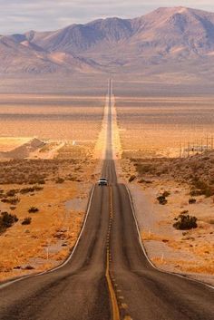 a car driving down an empty road in the middle of nowhere with mountains in the background