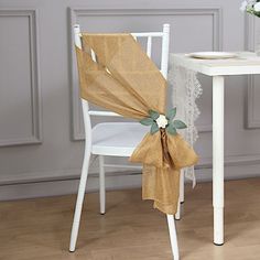 a chair with a bow on it next to a white table and flower vases