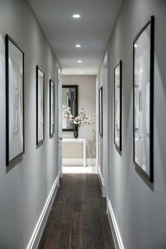 a long hallway with pictures on the wall and framed photographs on the walls, along with vases filled with flowers