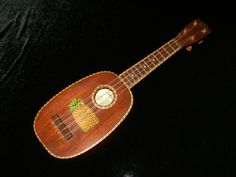 a wooden ukulele with pineapples on the fretboard and strings