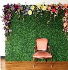 a chair sitting in front of a green wall with flowers on the grass behind it