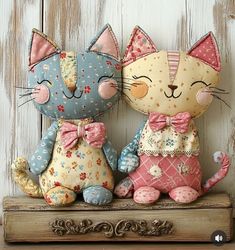 two stuffed cats sitting next to each other on top of a wooden shelf in front of a white wall