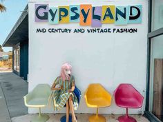 a woman with pink hair sitting on a chair in front of a store called gypsyland