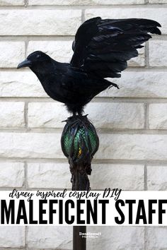 a black bird sitting on top of a metal pole next to a white brick wall