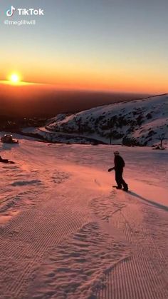 two people are snowboarding down a hill at sunset