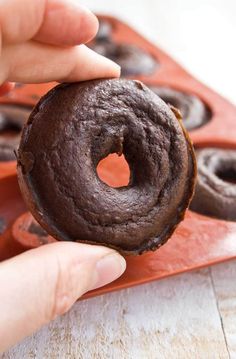 a person holding a chocolate doughnut in their hand