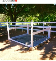 a white fenced in area with rocks and gravel on the ground next to trees