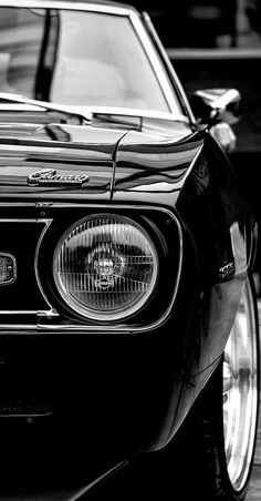 a black and white photo of the front end of a classic muscle car with its lights on