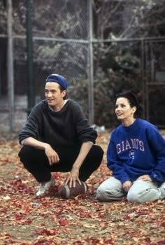 a man and woman sitting on the ground next to each other with leaves all over them