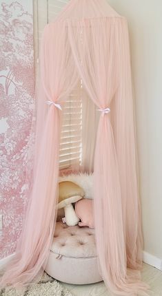 a pink canopy bed in the corner of a room with pillows and blankets on it