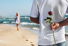 a man and woman walking on the beach with a rose in their hand