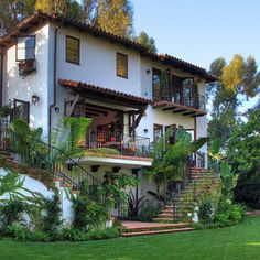 a large white house sitting on top of a lush green hillside next to a forest