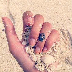 a person's hand holding sand and shells in the sand with a ring on it