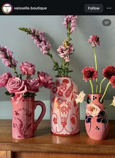 three pink vases with flowers in them on a wooden table next to a wall