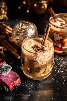 two glasses filled with liquid and cinnamon sticks on top of a table next to christmas decorations