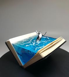 an open book sitting on top of a table next to a bird flying over the water