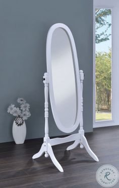 a white standing mirror on top of a wooden floor next to a vase with flowers