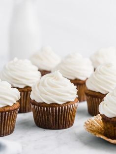 several cupcakes with white frosting sitting on a table