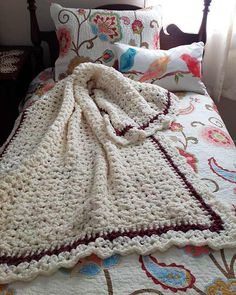 a crocheted blanket on top of a bed next to pillows and pillow cases