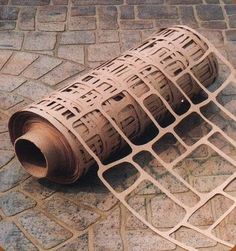 a piece of metal mesh sitting on top of a stone floor next to a brick wall