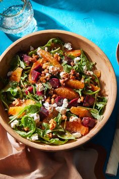 a wooden bowl filled with salad on top of a blue cloth next to a glass of water