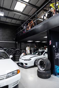 two white sports cars parked in a garage next to each other with people looking at them